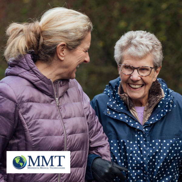 Image shows older woman and female caregiver laughing together in outdoor environment